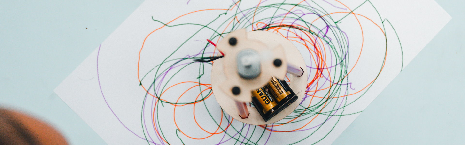 A student-made drawing machine surrounded by colorful looping lines on paper